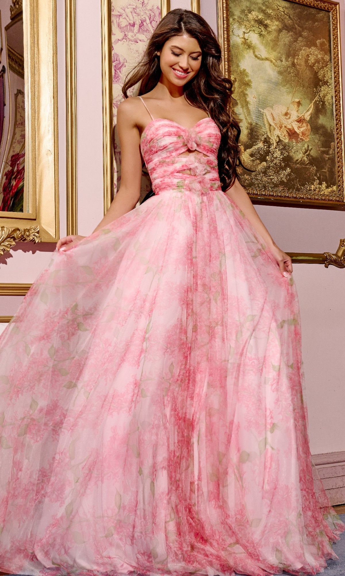 A woman in a strapless red floral-print Jovani 40402 prom dress stands indoors, smiling as she holds out the skirt of her a-line gown. Ornate framed paintings are displayed on the wall behind her.
